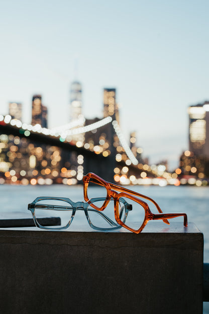 Espejuelos acetato japonés anaranjadas y gris transparente sobre un muro con el Brooklyn Bridge de fondo